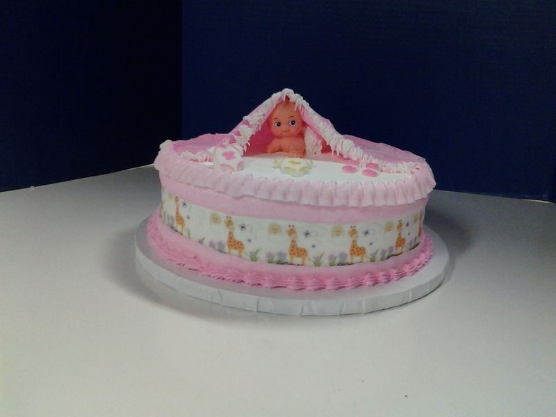 Baby shower cake with pink frosting, a giraffe pattern, and a baby doll topper.
