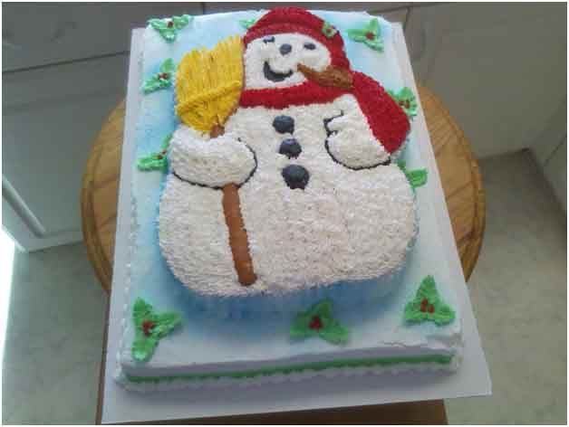 Snowman cake with red hat and scarf, holding a broom, on a blue frosted base.