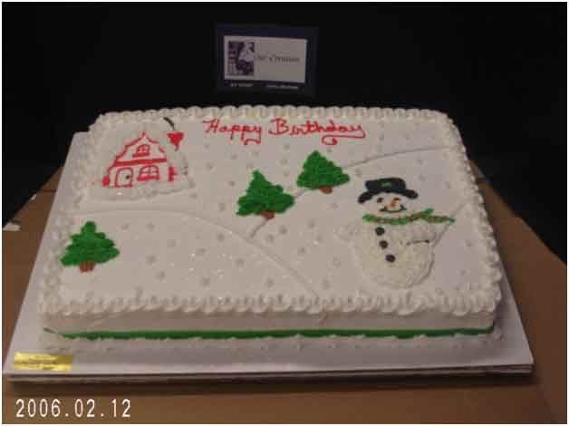 Birthday cake decorated with a winter scene: house, snowman, evergreen trees, and 