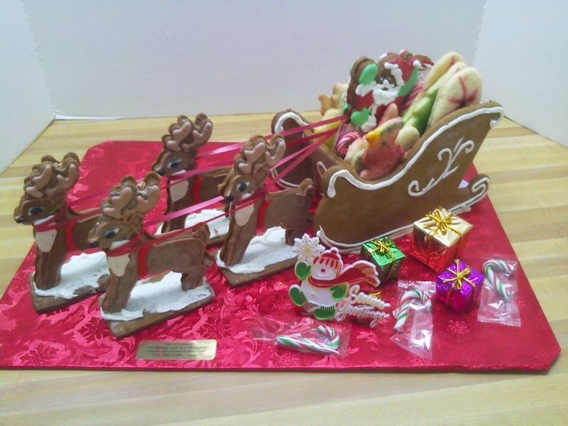 Gingerbread Santa's sleigh with reindeer, gifts, and snowman on a red patterned base.