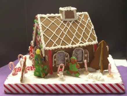 Gingerbread house decorated with icing, candy, and trees. Set on a white base with red and white candy cane trim.
