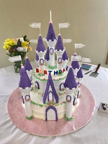 Birthday cake decorated as a fairytale castle; white and purple with flags, flowers, and 