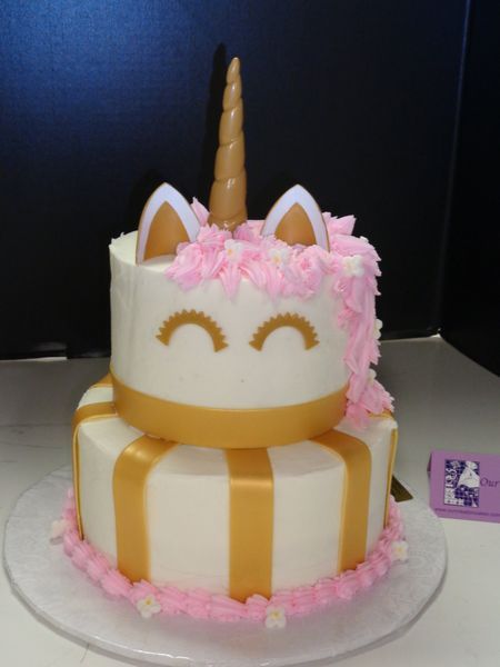 Two-tiered unicorn cake with gold accents, pink frosting mane, and a golden horn.
