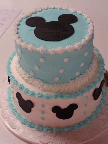 Two-tiered cake with blue frosting and Mickey Mouse silhouettes and polka dots.