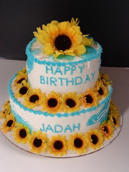 Two-tiered birthday cake decorated with sunflowers, blue frosting accents, and the words 