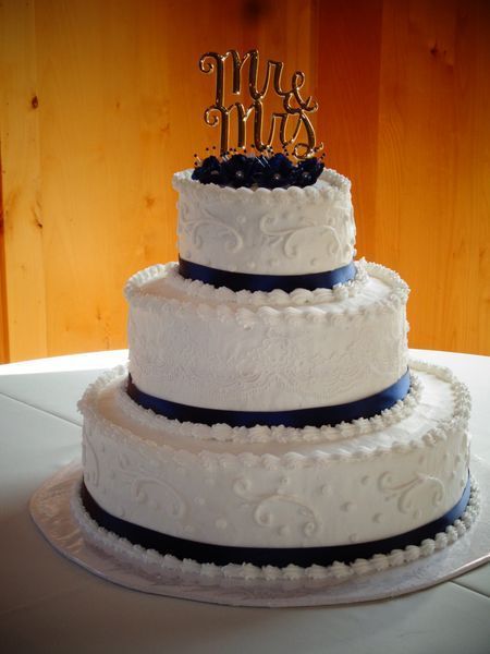 Three-tiered white wedding cake with navy blue ribbons and a 