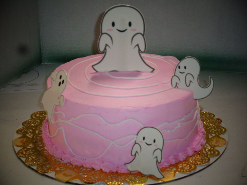 Pink frosted cake with cartoon ghost decorations.
