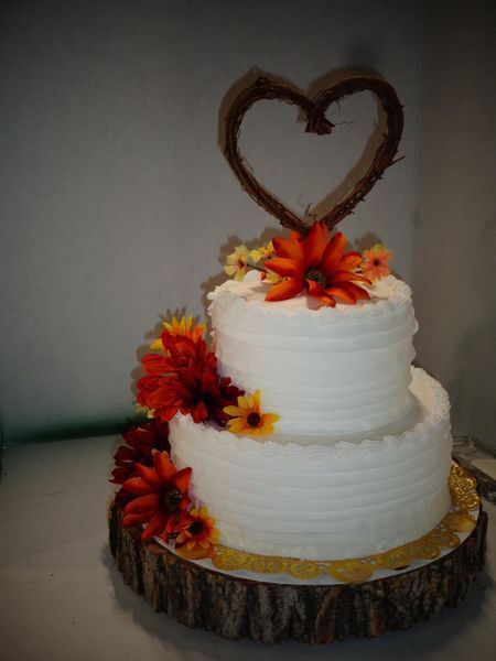 Two-tiered white cake with orange flowers, a twig heart, and a wood base.