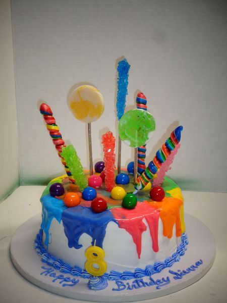 Birthday cake with colorful frosting drips, topped with lollipops and gumballs, and a candle that says “8”.