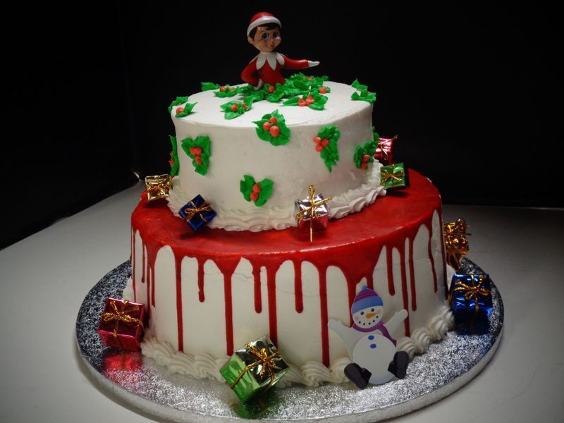 Two-tiered Christmas cake with red icing drip, presents, holly, and Elf on the Shelf topper.