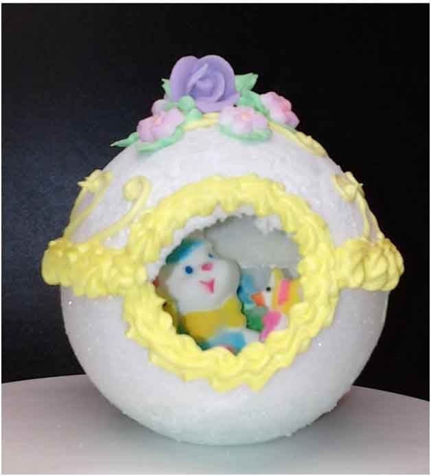 Decorated sugar Easter egg with yellow frosting trim and two bunny figures inside.