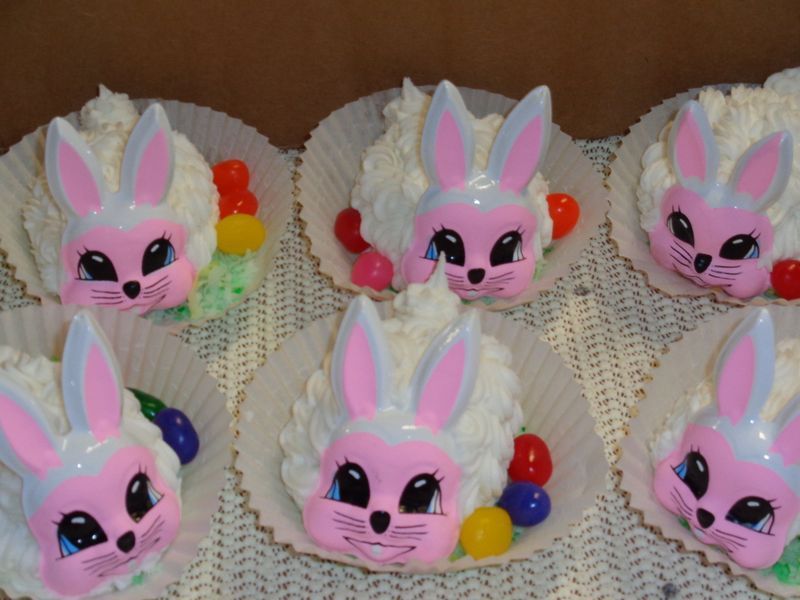 Six bunny cupcakes with white frosting, pink faces, and jelly beans.