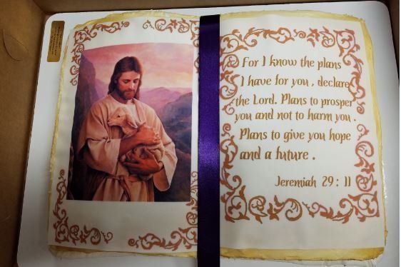 Cake decorated as an open book, with a picture of Jesus holding a lamb, and a Bible verse.