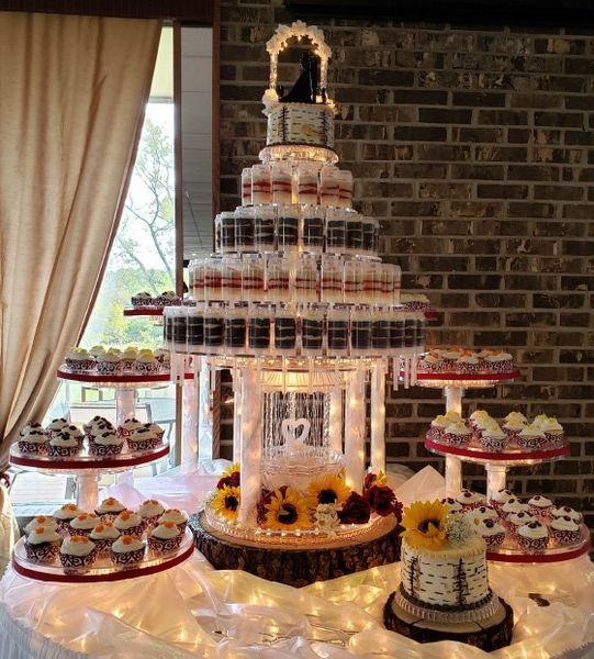 Wedding cupcake tower with small cake. Sunflowers and string lights on a table against a brick wall.