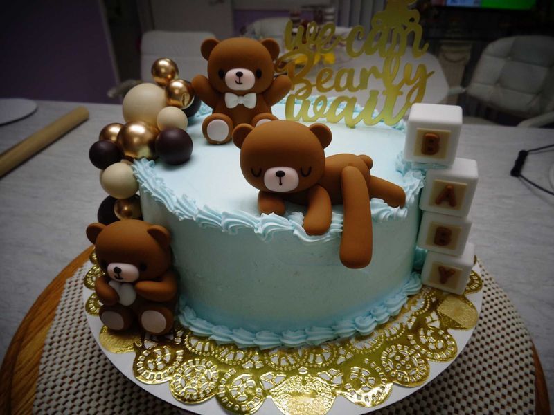 Cake with teddy bear decorations for a baby shower. Light blue frosting, gold accents, ABC blocks, and brown bears.