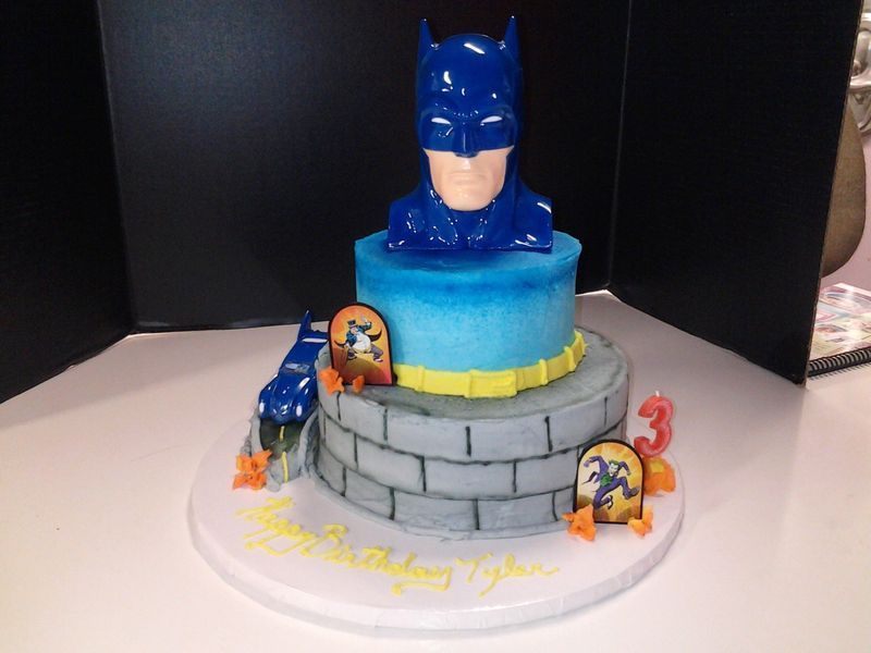 Batman-themed birthday cake with a blue figure, brick-like base, candles, and 