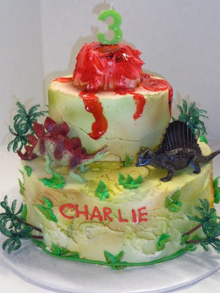 Two-tiered dinosaur-themed birthday cake with volcano, dinosaurs, and 