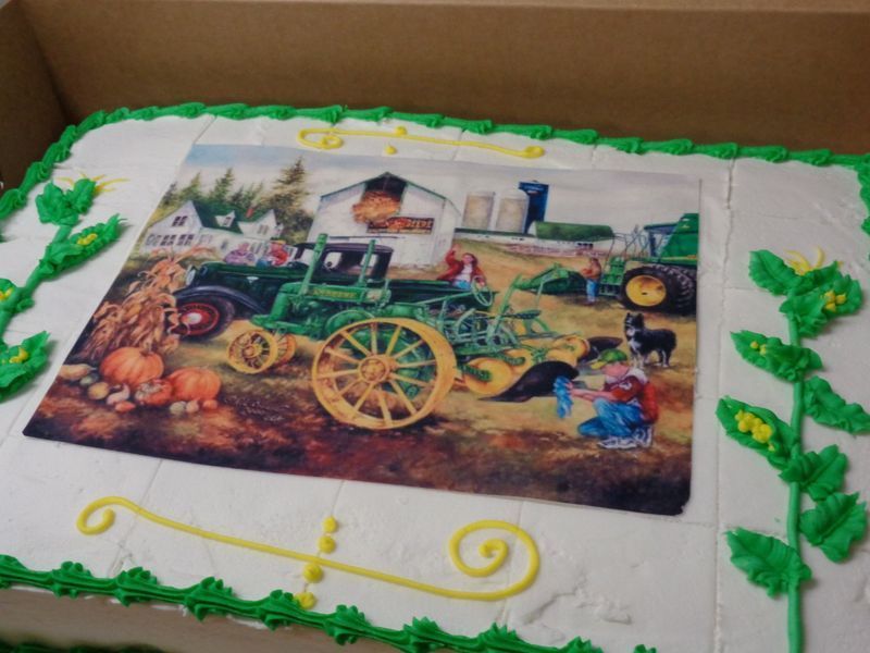 Cake decorated with a farm scene; green tractor, pumpkins, barn, figures, green and yellow frosting details.