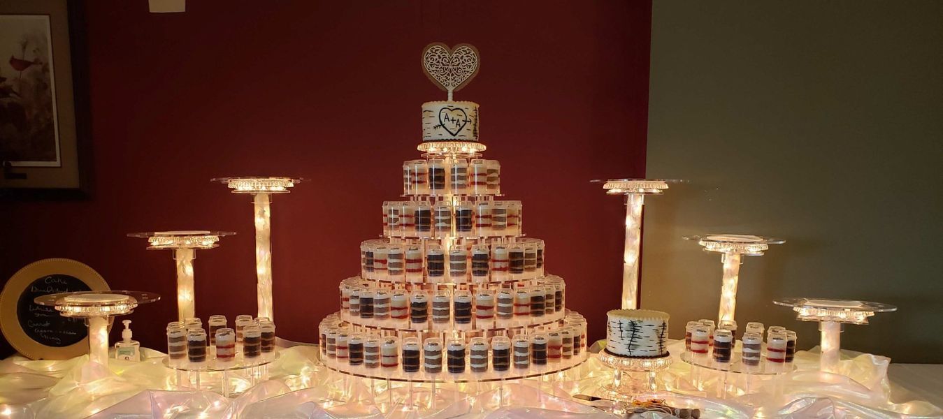 Cake display with multiple tiers of shot glasses, decorated with lights and a heart topper.