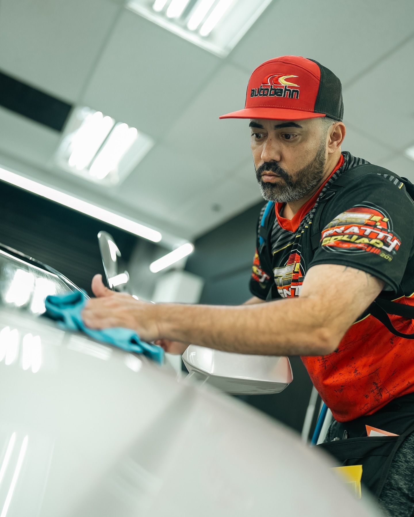 A man wearing a red hat is cleaning a car with a cloth.