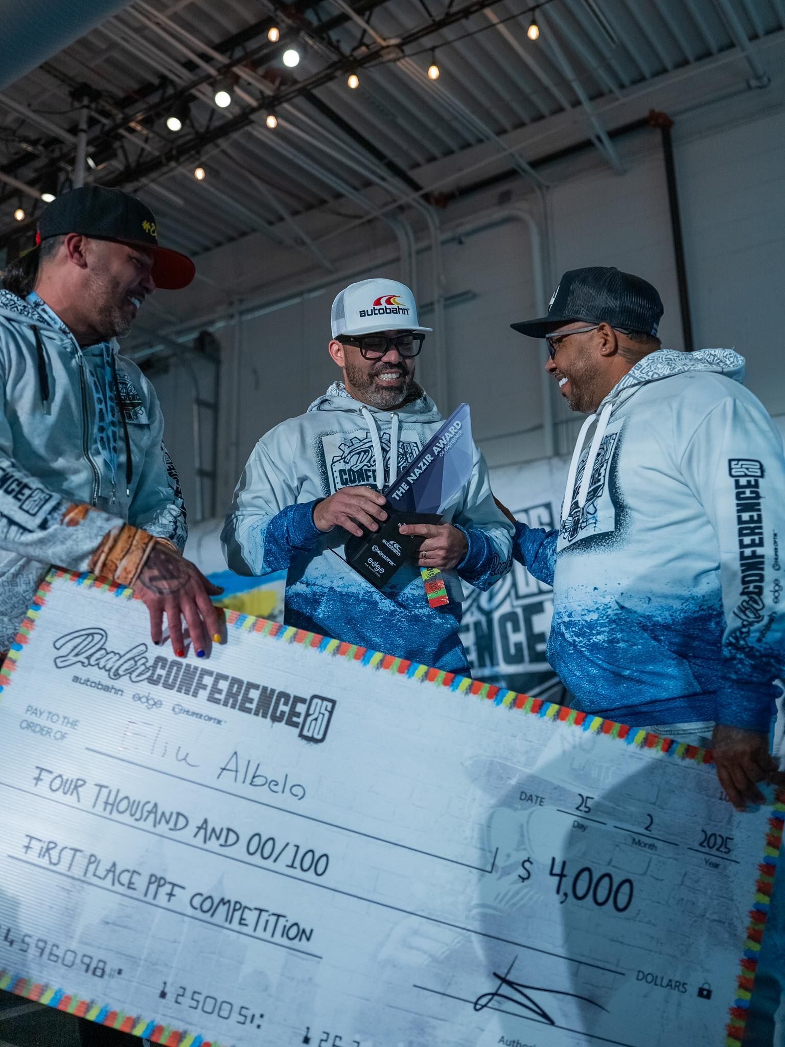 Three men are holding a large check in a room.