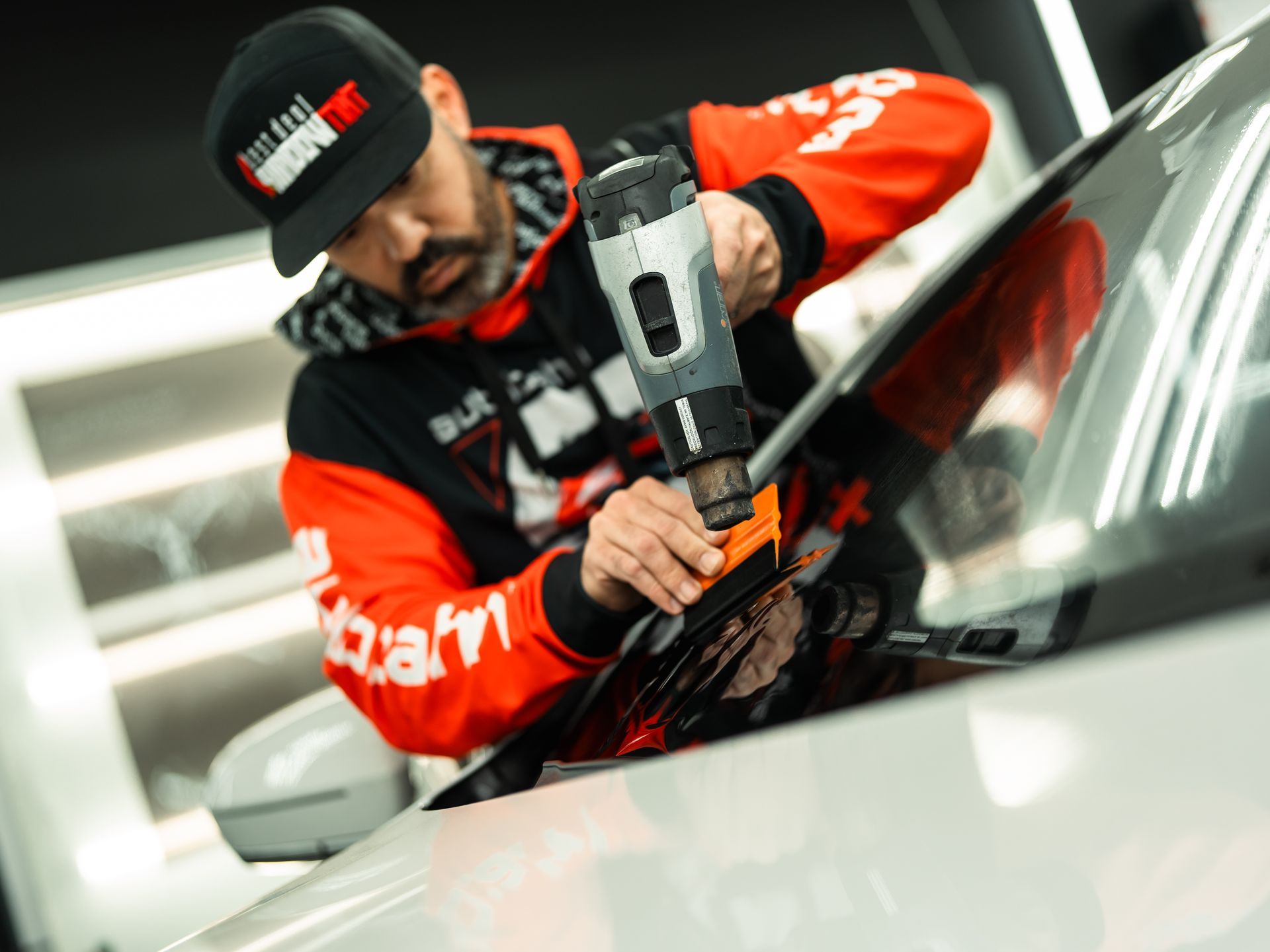 A man is working on a car windshield with a tool.