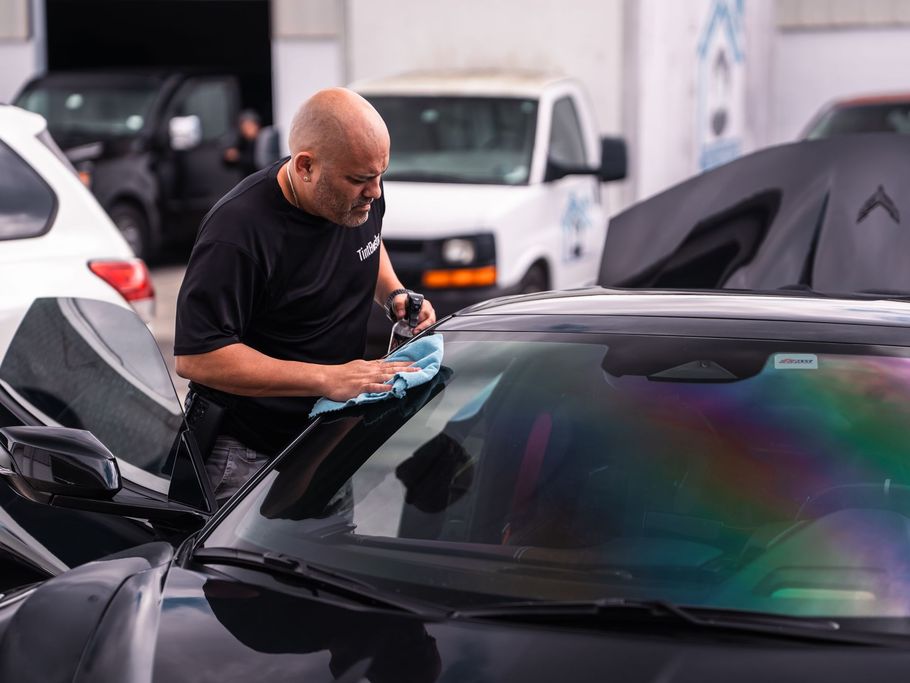 A man is cleaning the windshield of a car with a cloth.