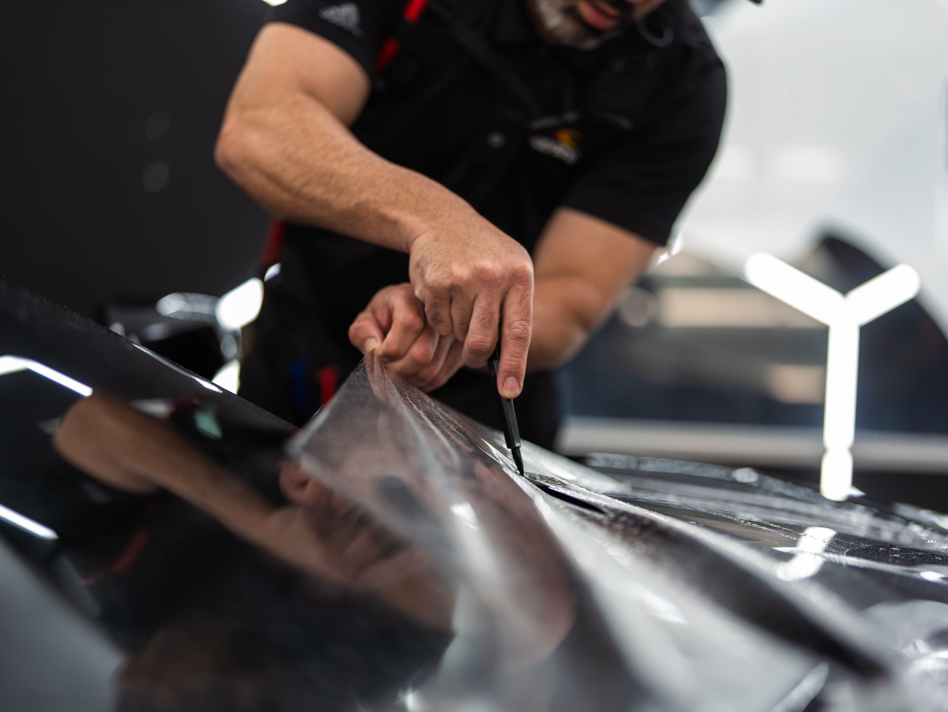 A man is applying a protective film to the hood of a car.