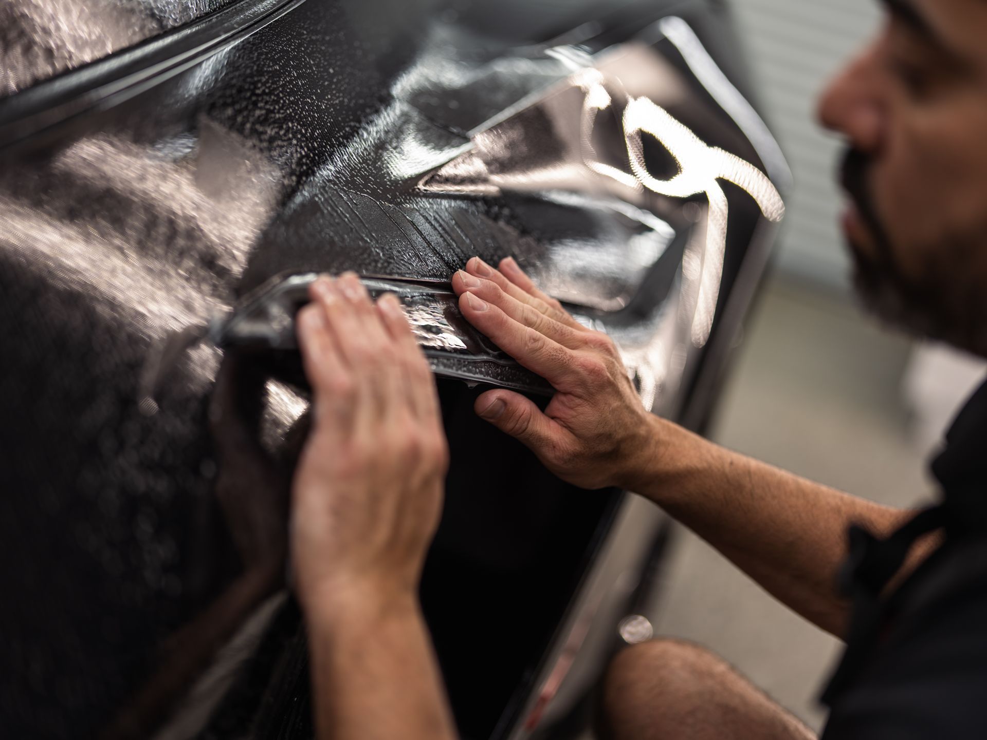 A man is wrapping a car with a piece of plastic.