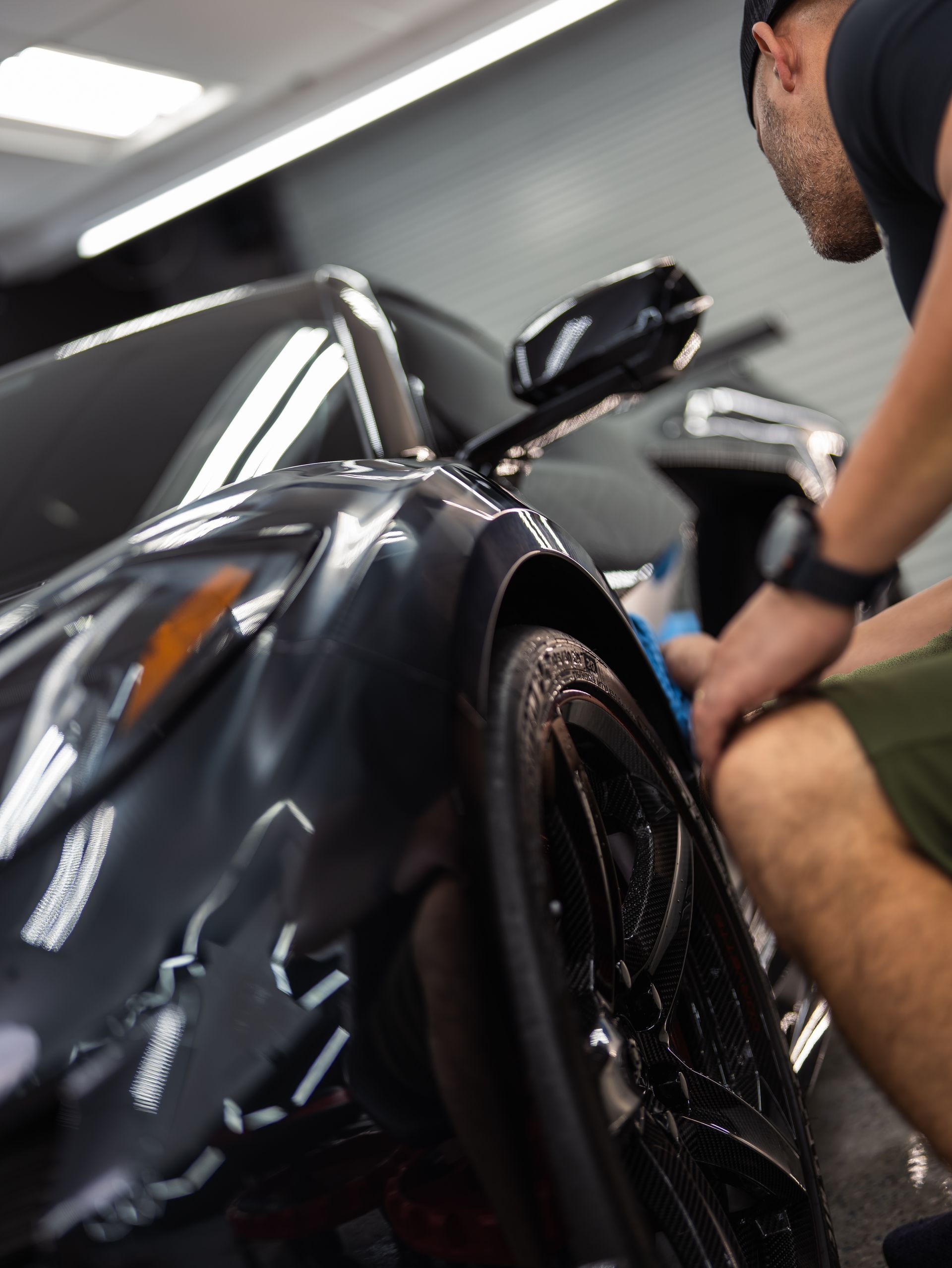 A man is cleaning the fender of a black sports car