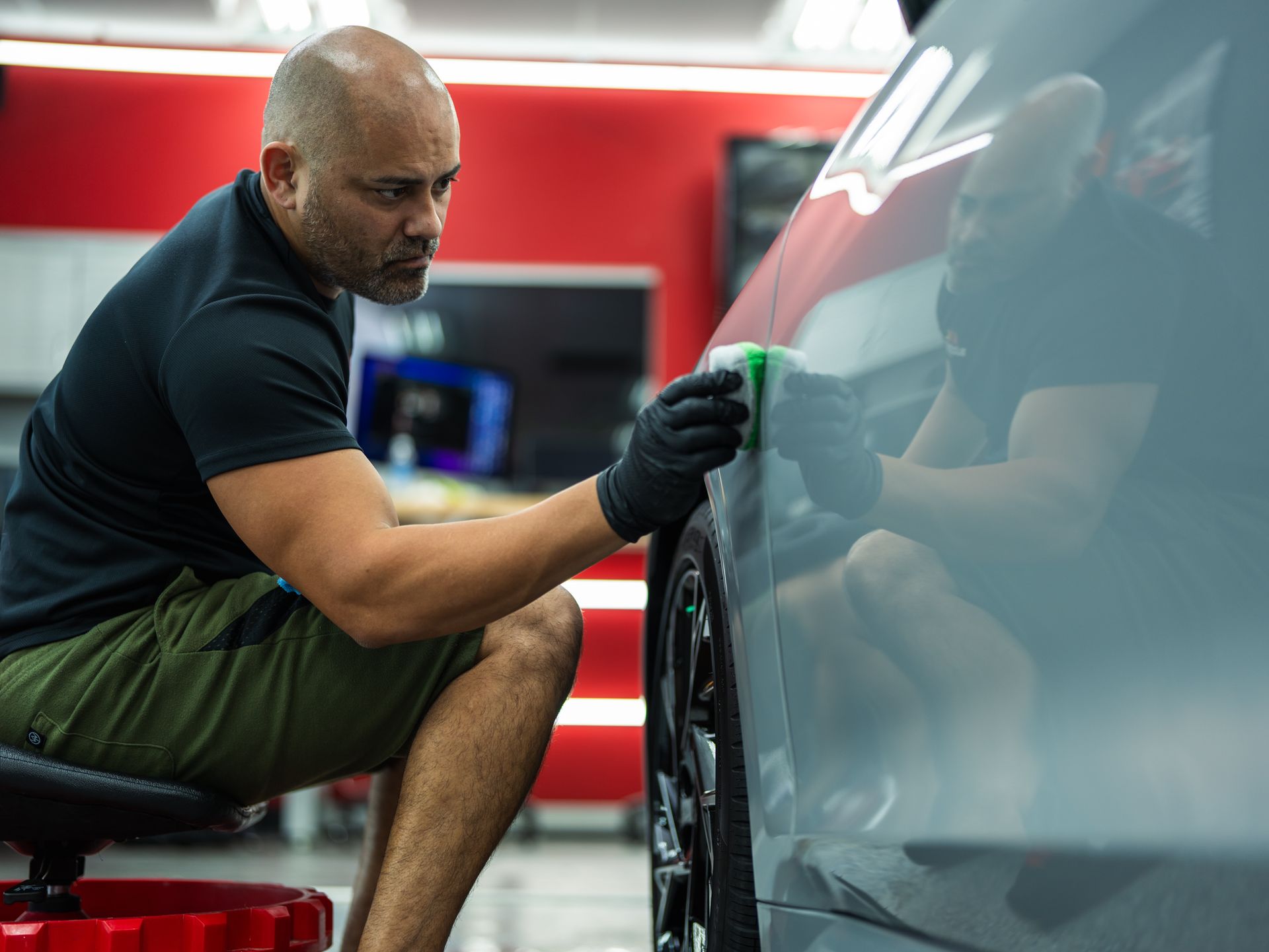 A man is cleaning the side of a car in a garage.