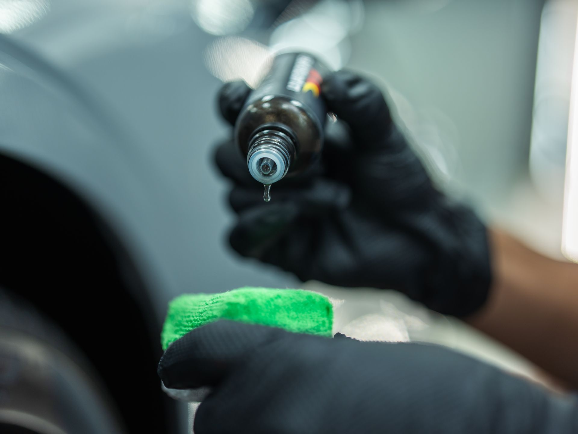 A person is holding a bottle of liquid and a green cloth.