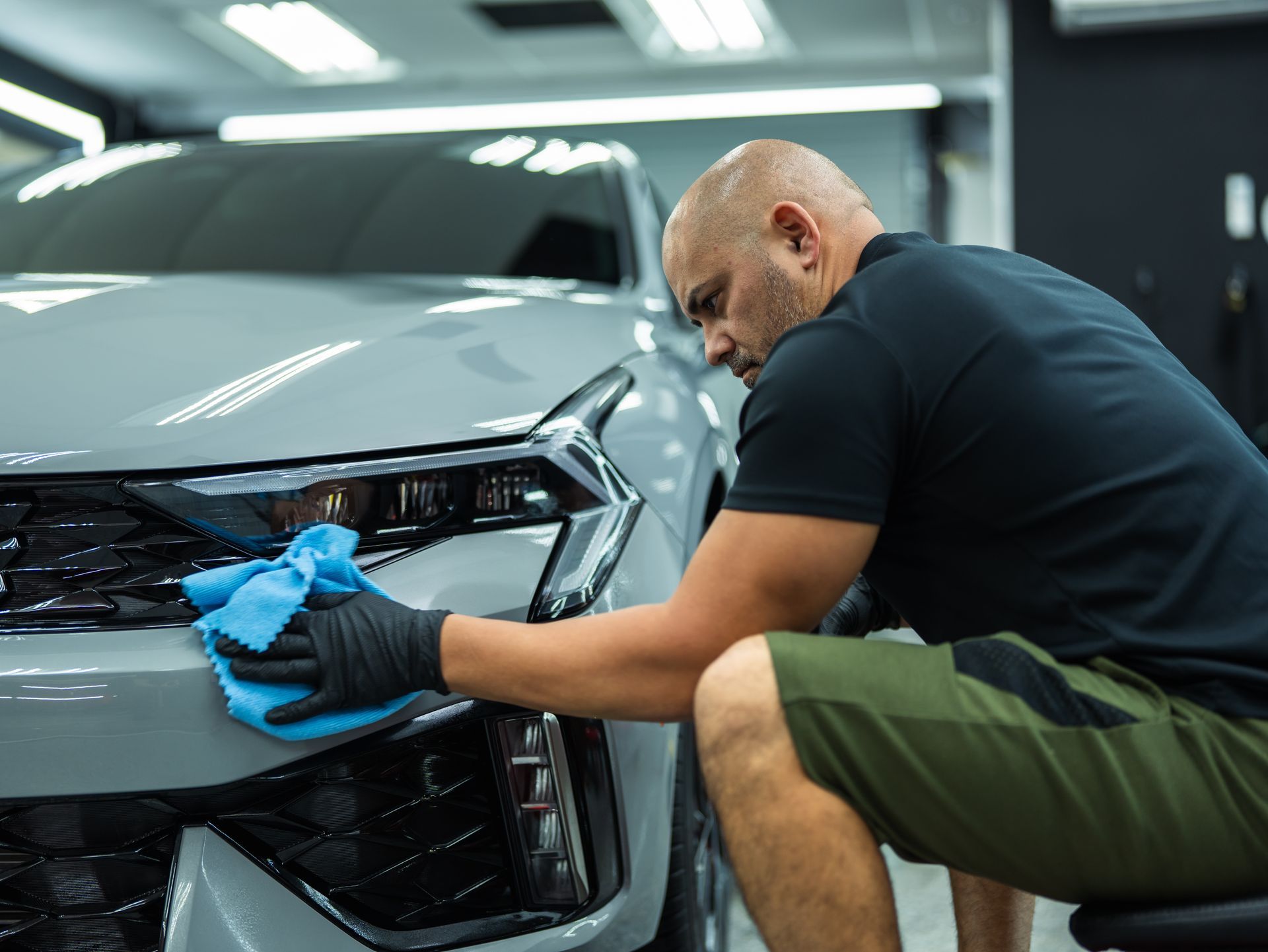 A man is cleaning the front of a car with a cloth.