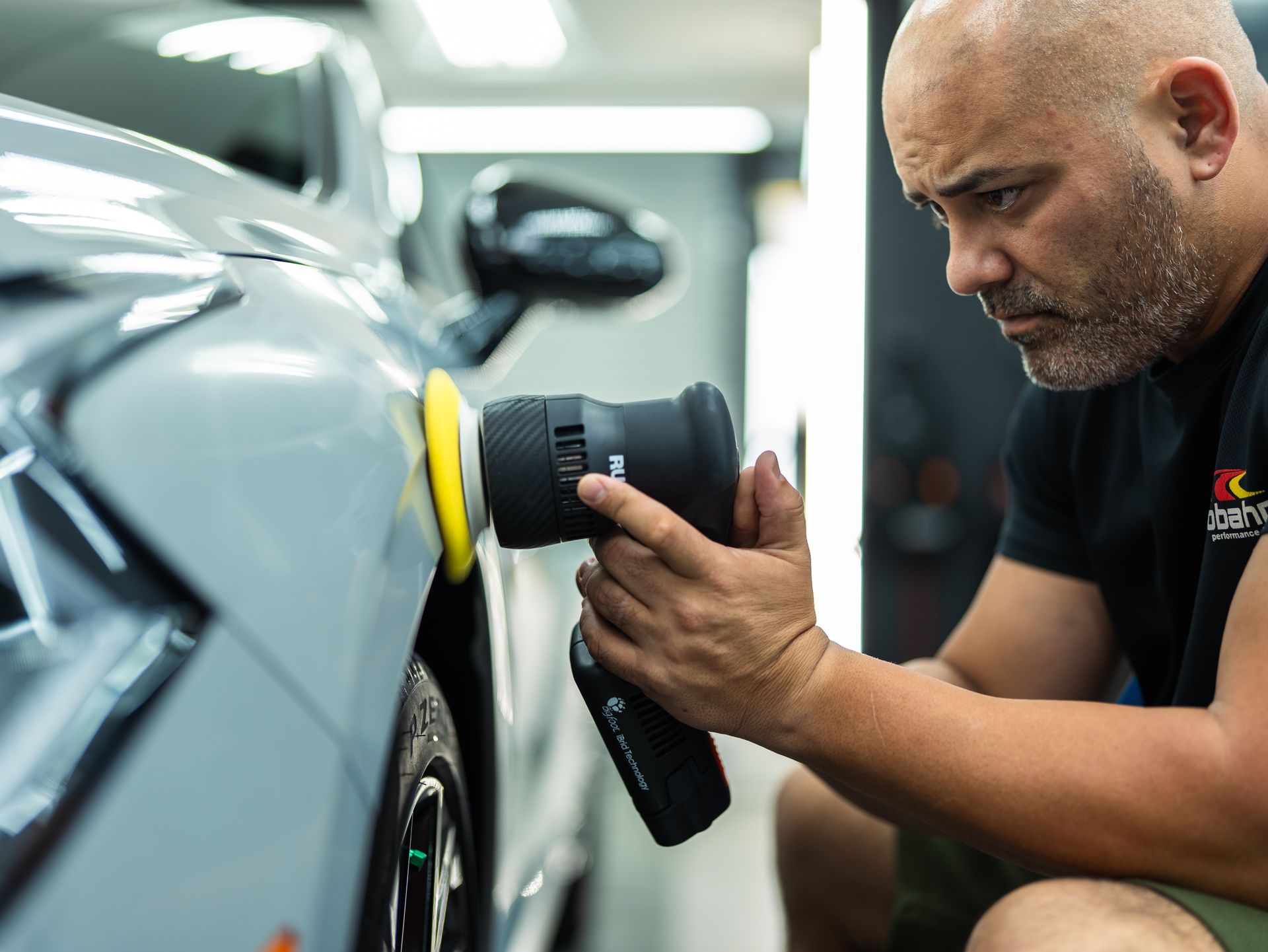 A man is polishing a car with a polisher in a garage.