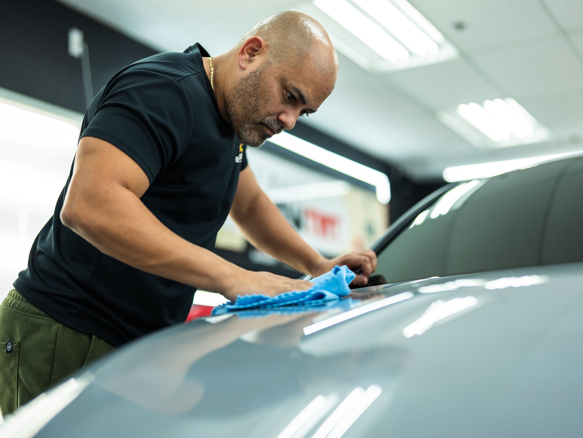 A man is cleaning the hood of a car with a cloth.