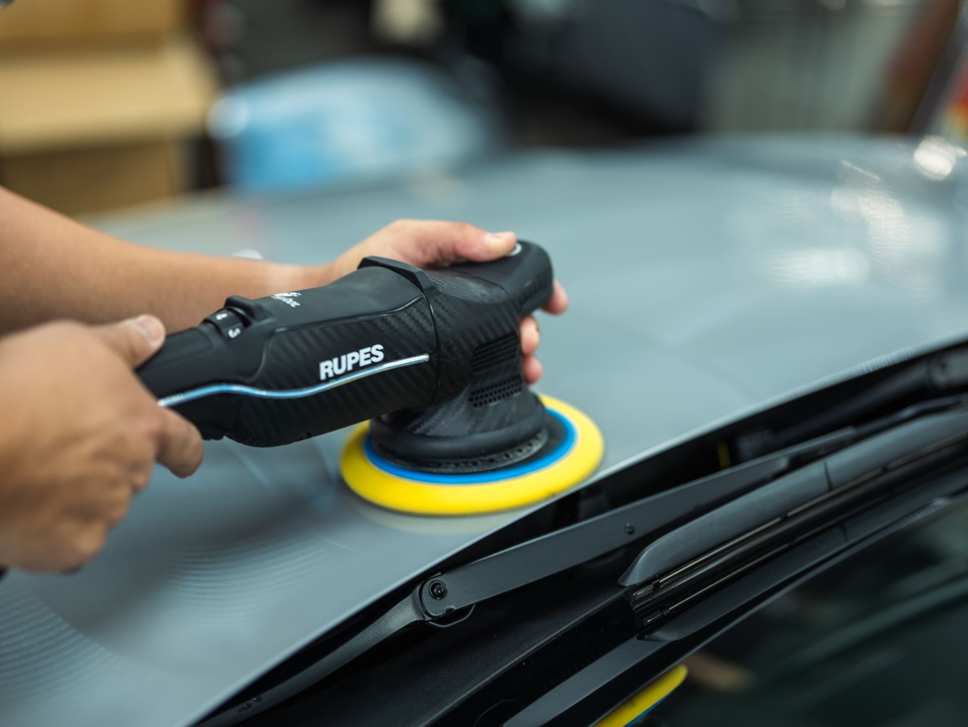 A person is polishing the hood of a car with a machine.