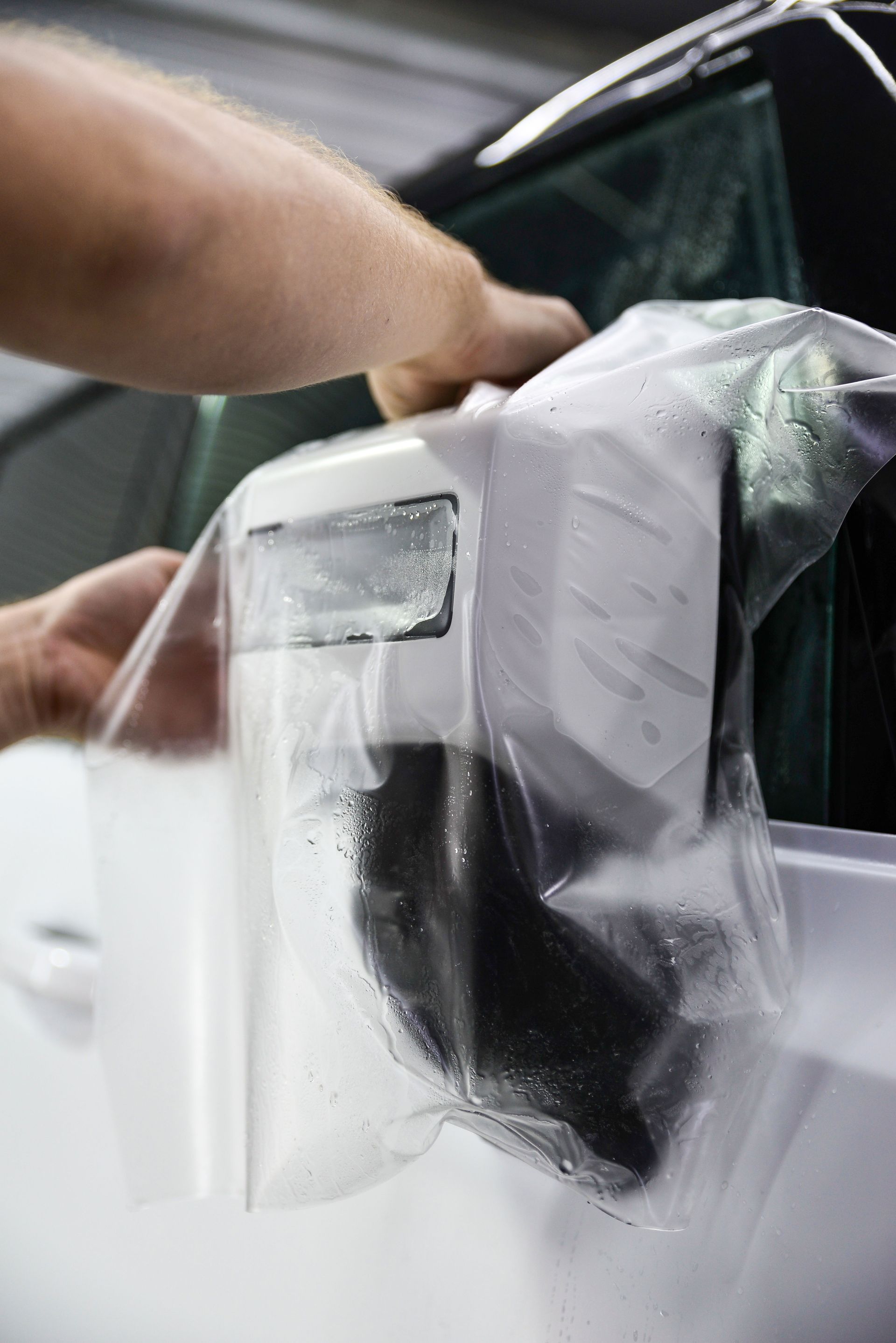 A person is putting a plastic bag on a car door.
