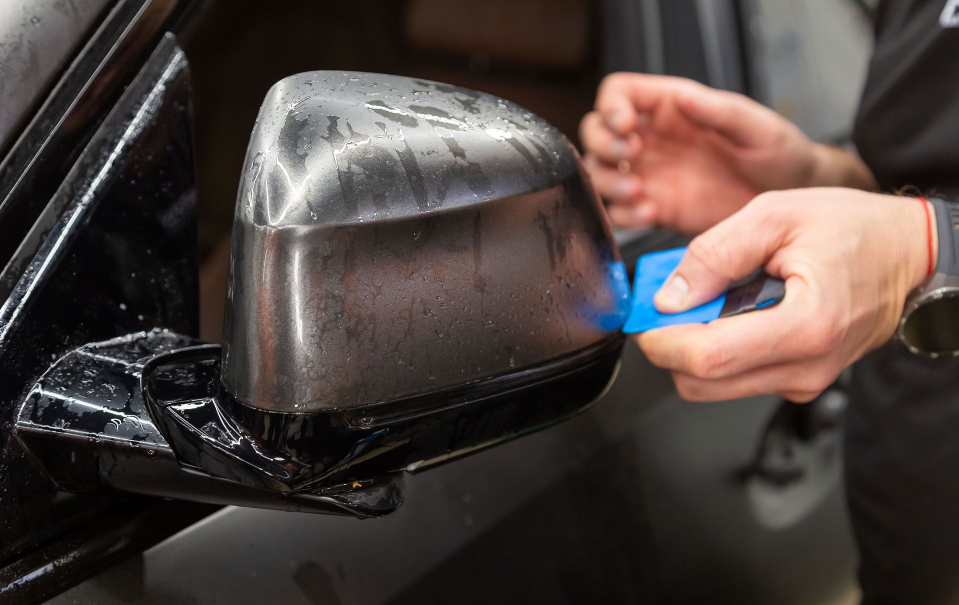 A person is wrapping a side view mirror with a film.