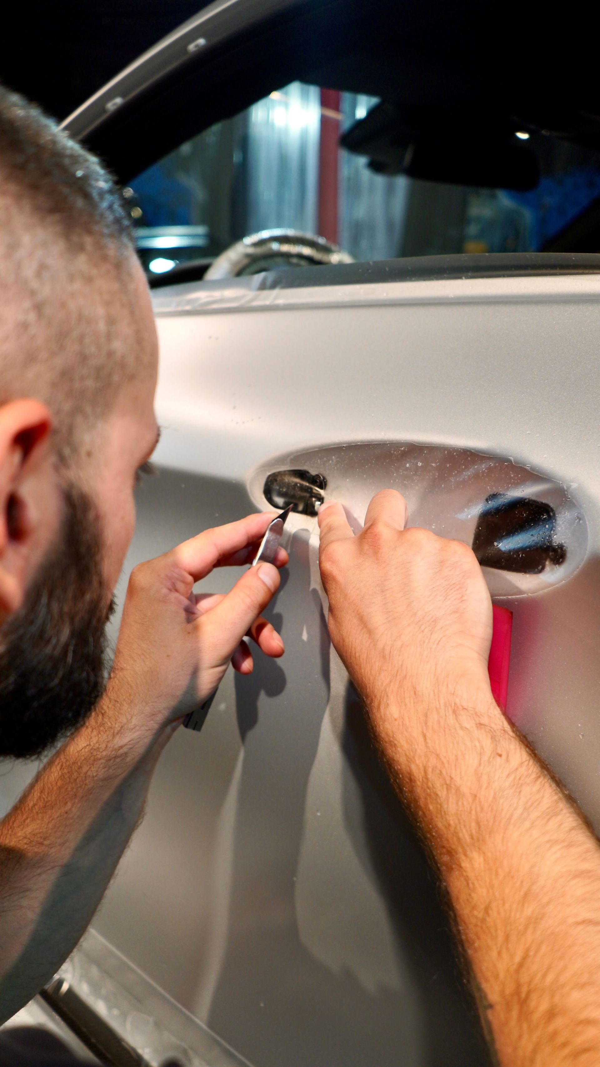 A man with a beard is working on the door of a car.