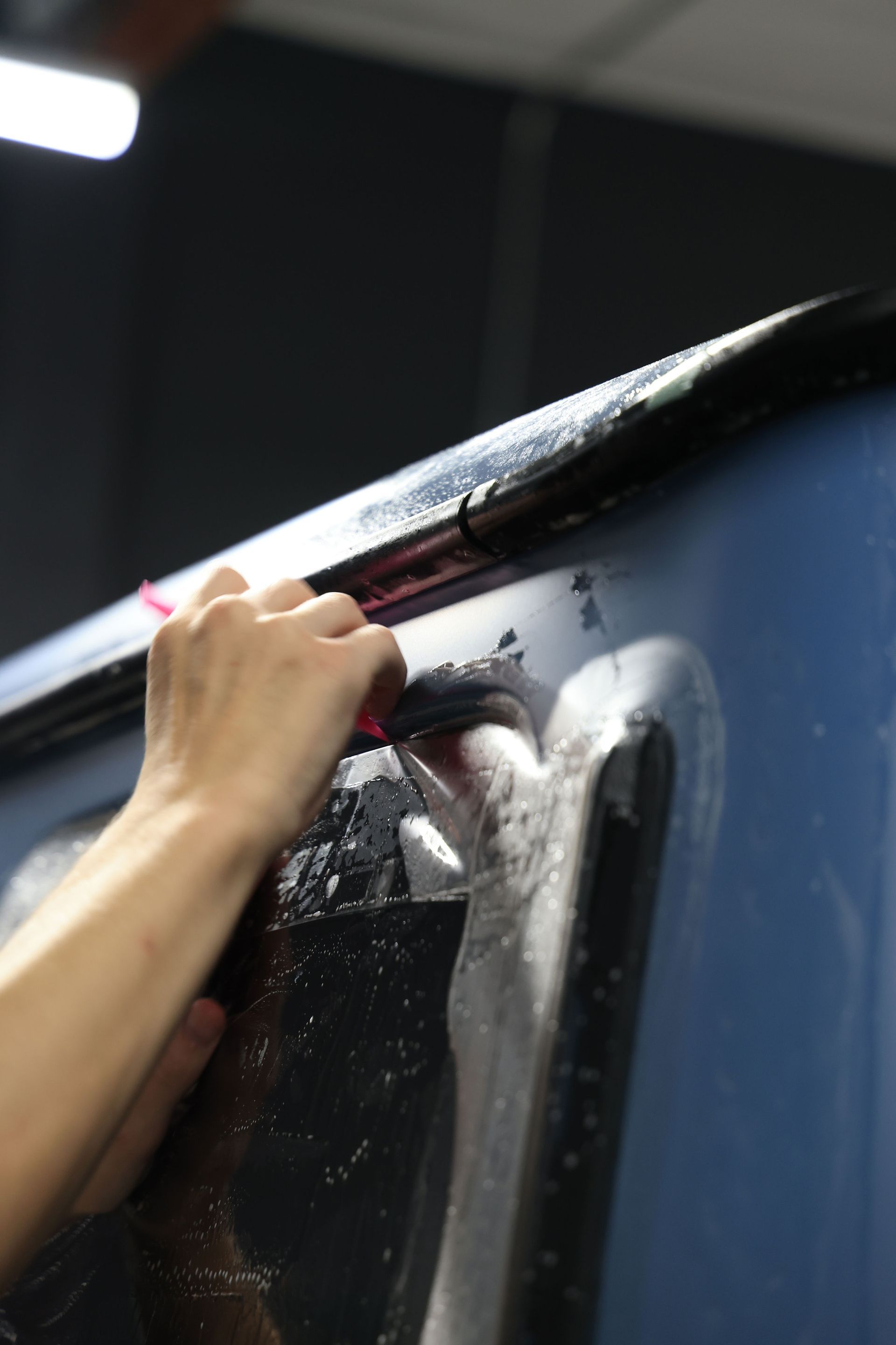 A person is applying tinted window film to a car window.