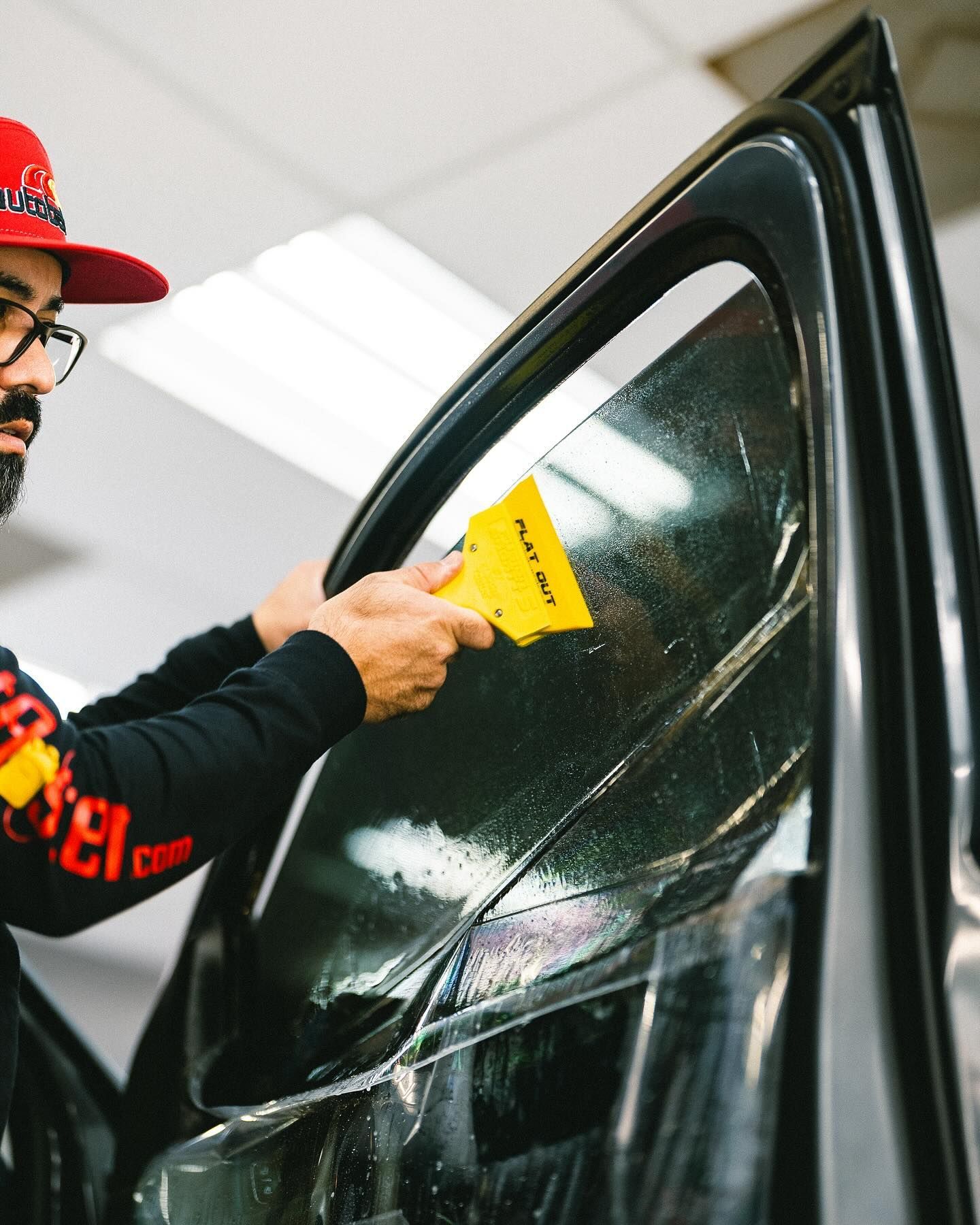 A man in a red hat is applying window tinting to a car.