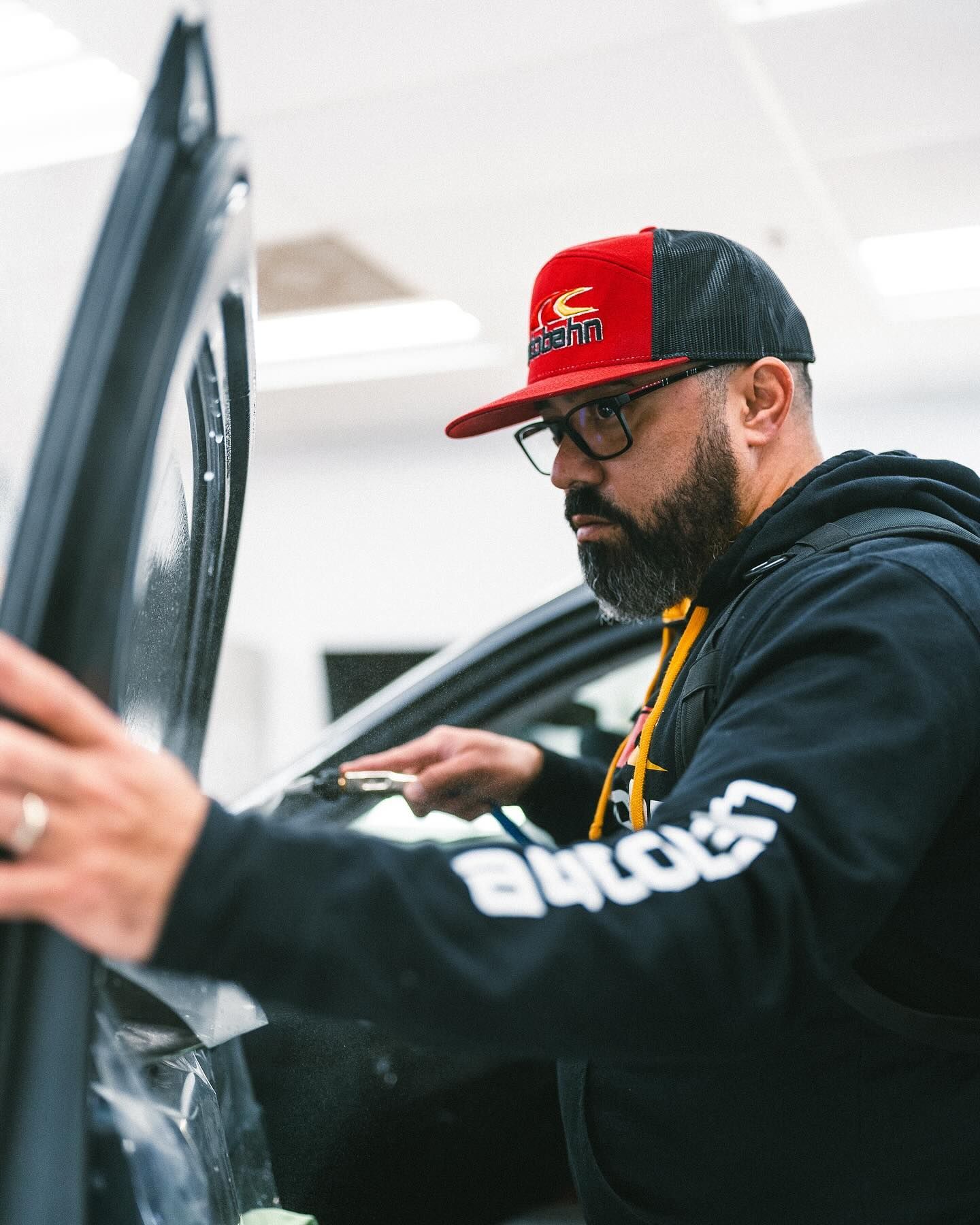 A man wearing a red hat and glasses is working on a car.