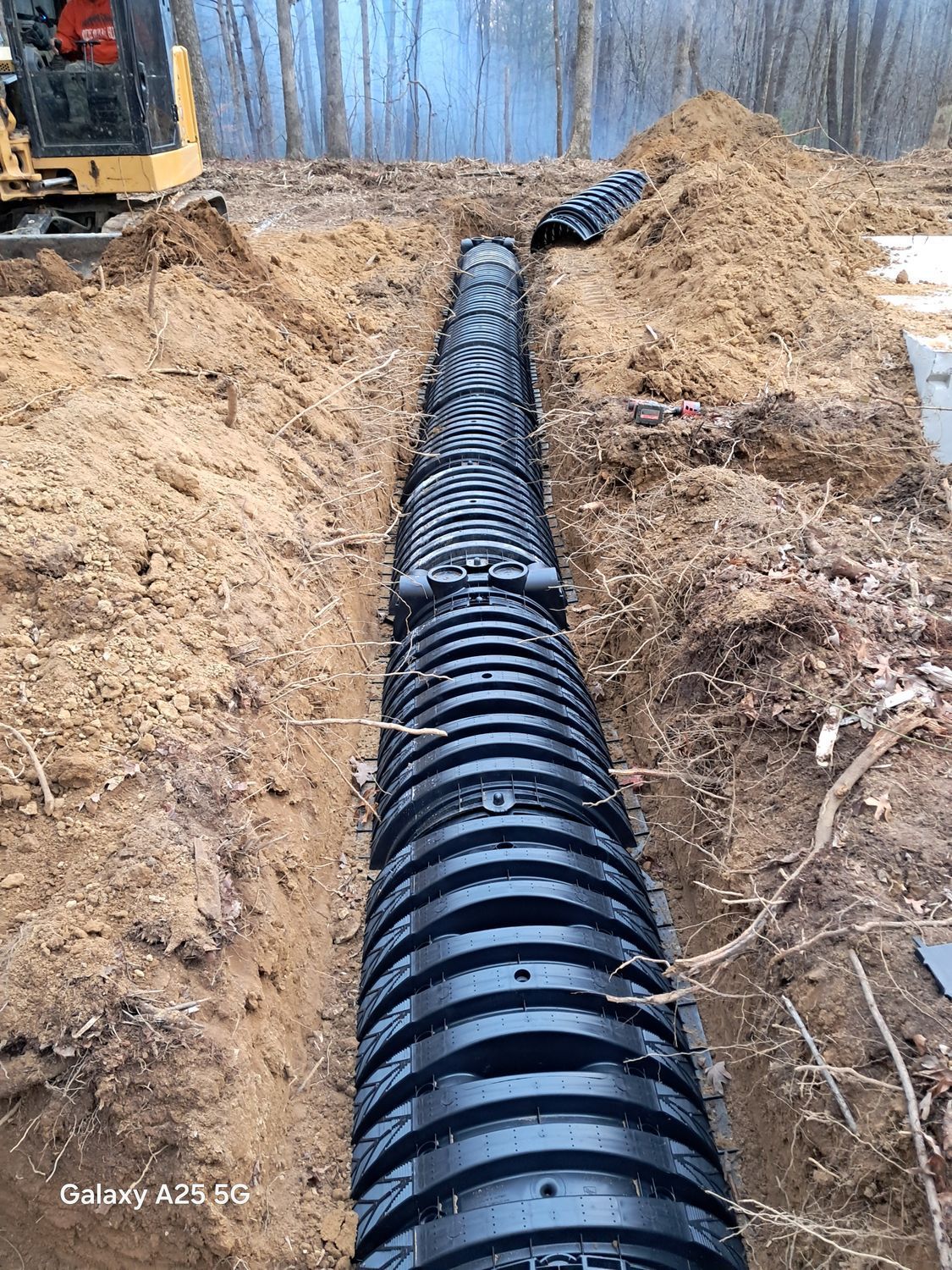 A large black pipe is being installed in the dirt