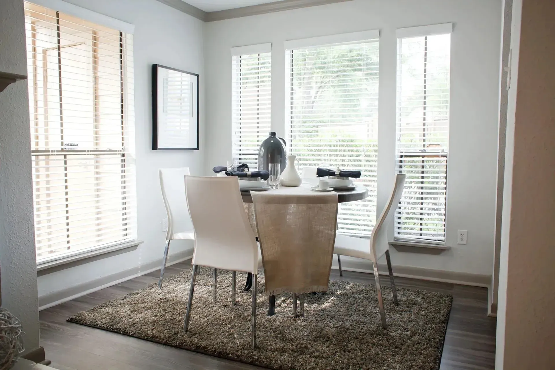 Modern dining area with a round table, white chairs, and window blinds.