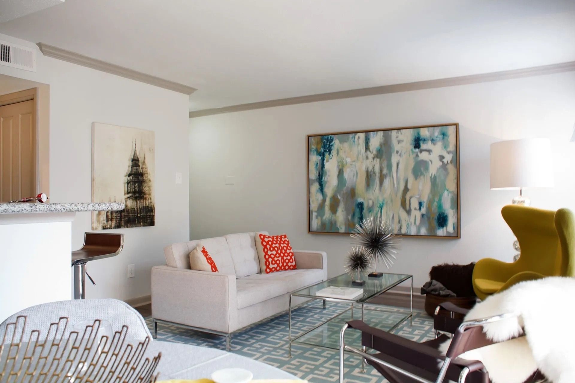 Living room in an apartment with a beige sofa, glass coffee table, and abstract wall art.
