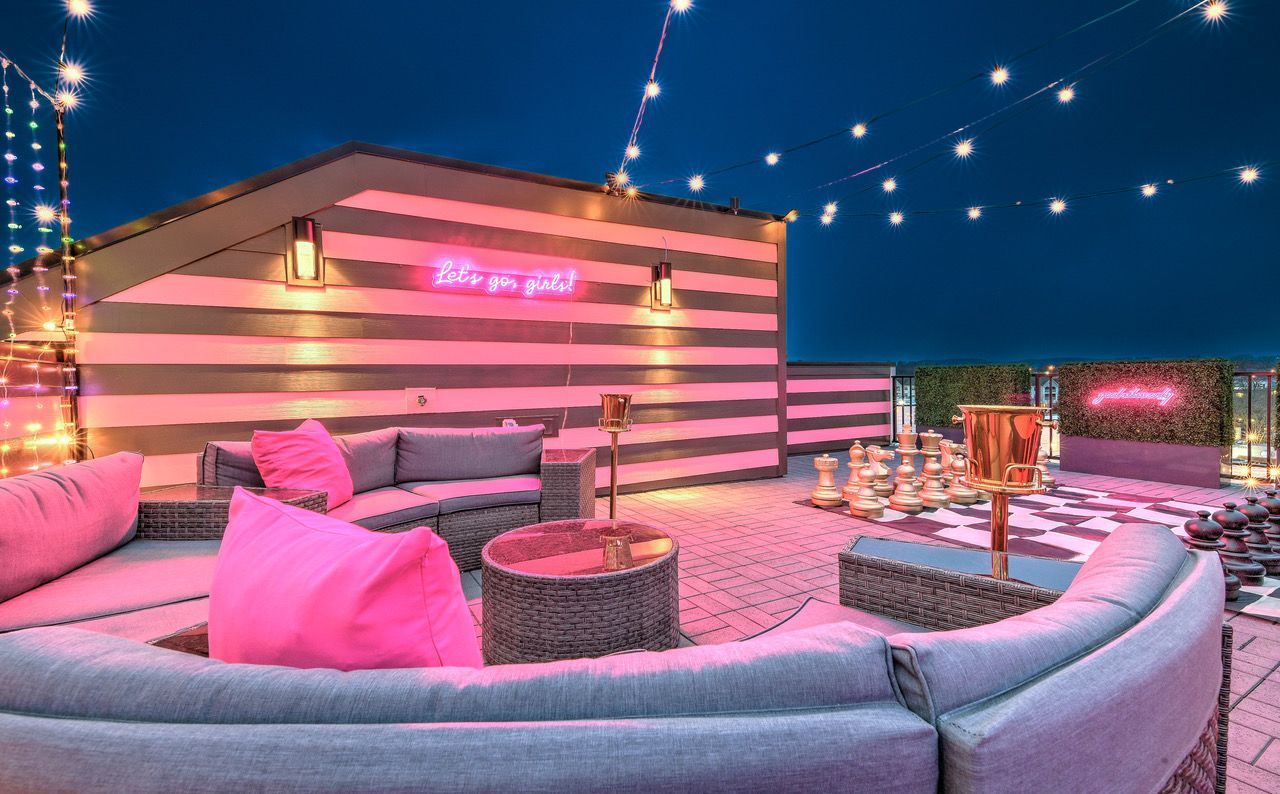 A patio with a couch , tables , and a neon sign.