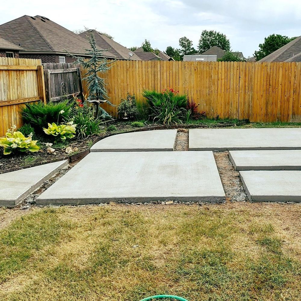 A backyard with concrete walkways and a wooden fence