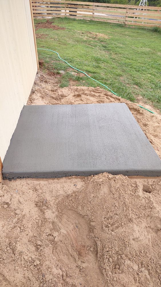 A concrete slab is sitting on top of a pile of dirt next to a house.