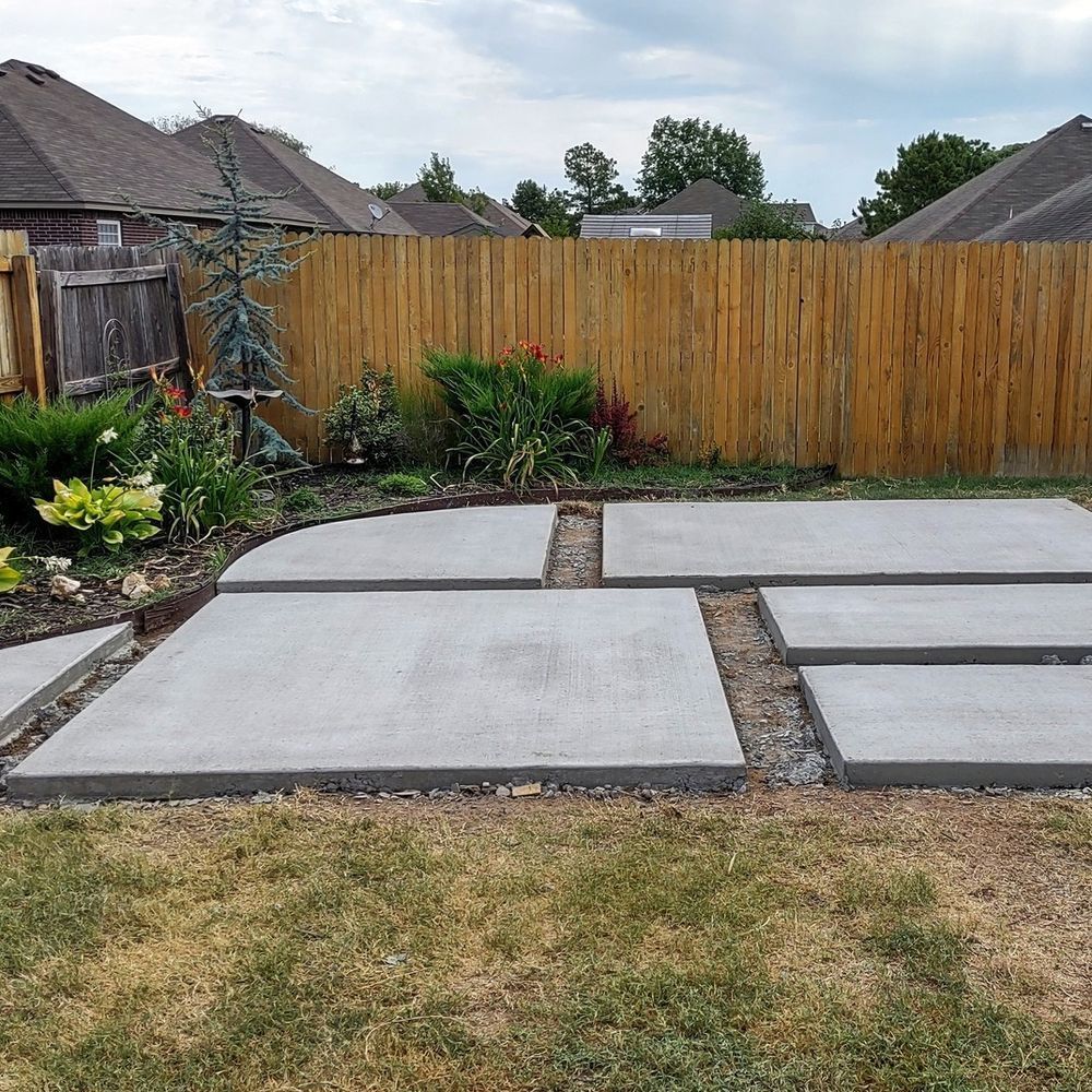 A concrete walkway in a backyard with a wooden fence in the background.