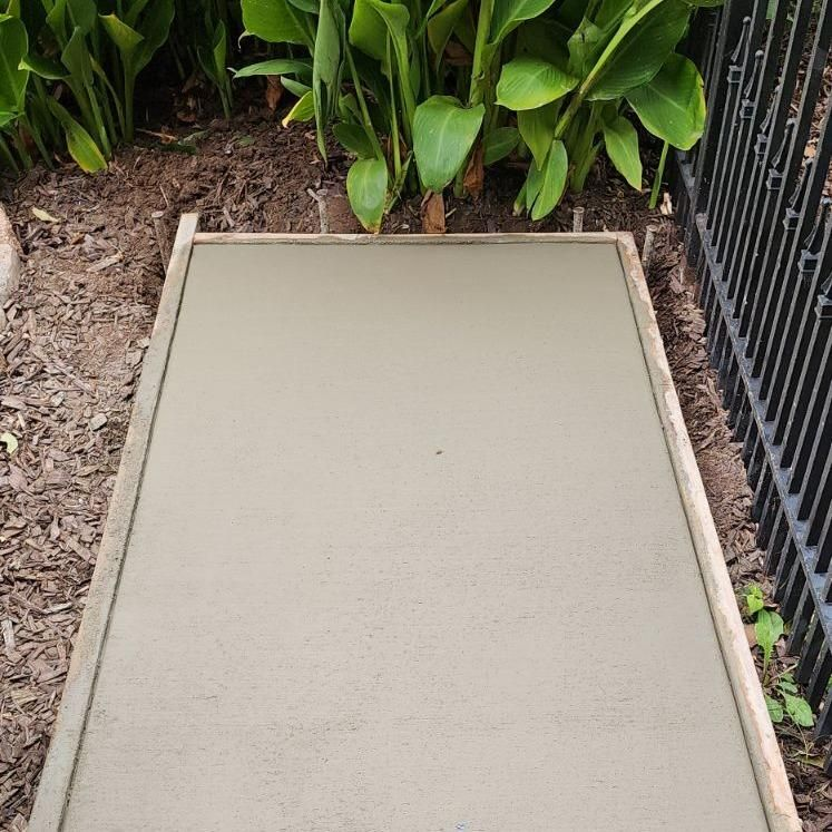A concrete walkway is being built in a garden next to a fence.